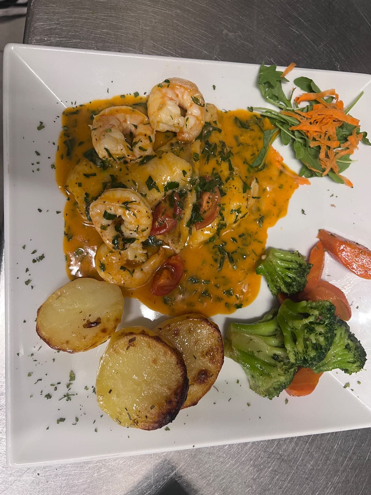 Garnelen und Fischfilet in Kräutersauce mit Ofenkartoffeln, Brokkoli und Karotten auf einem weißen Teller