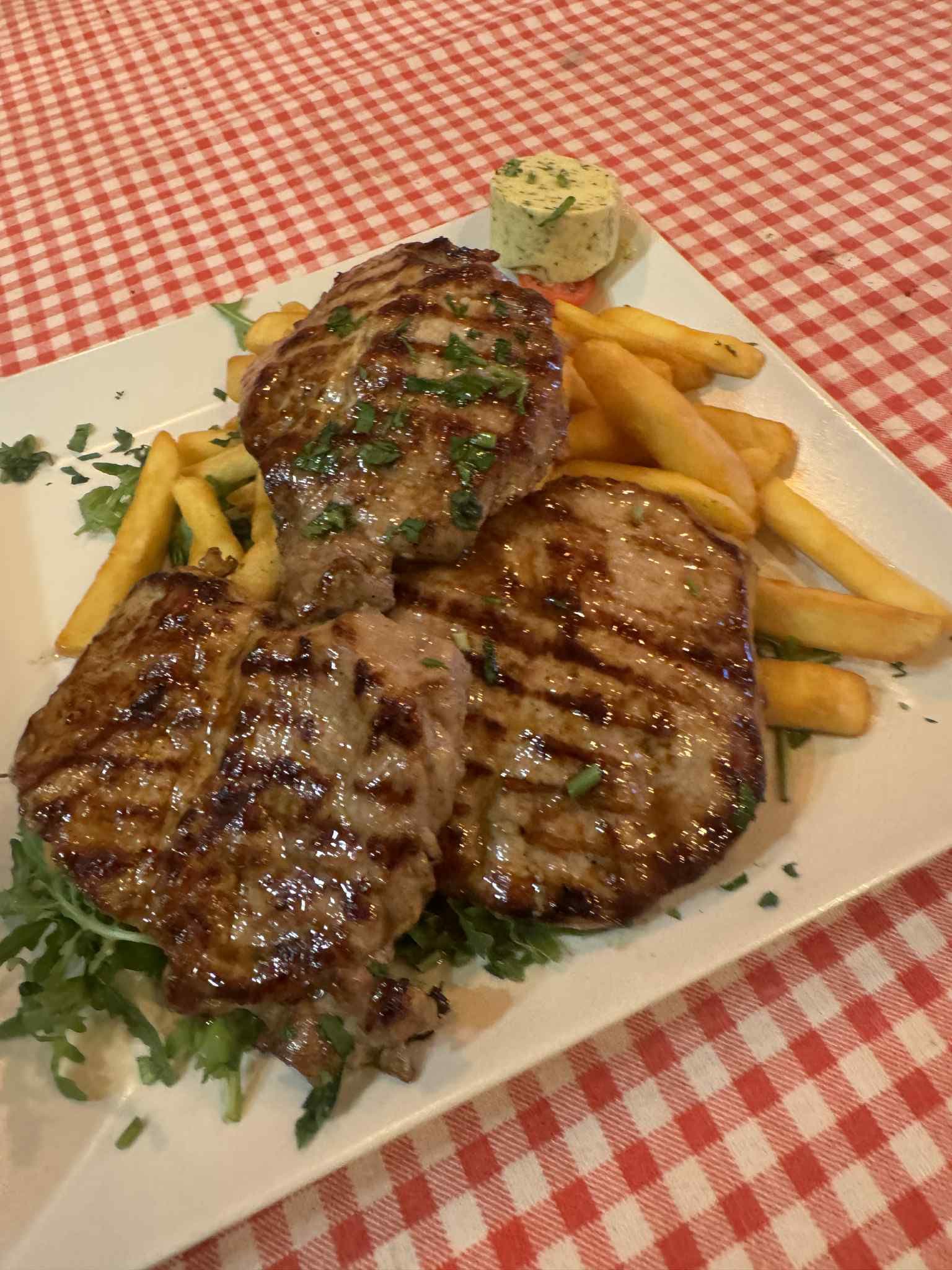 Pollo alla Griglia: gegrilltes Hähnchenbrustfilet mit Pommes, Rucola und Kräuterbutter auf einem weißen Teller